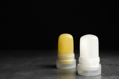 Photo of Natural crystal alum deodorants on grey marble table against black background. Space for text