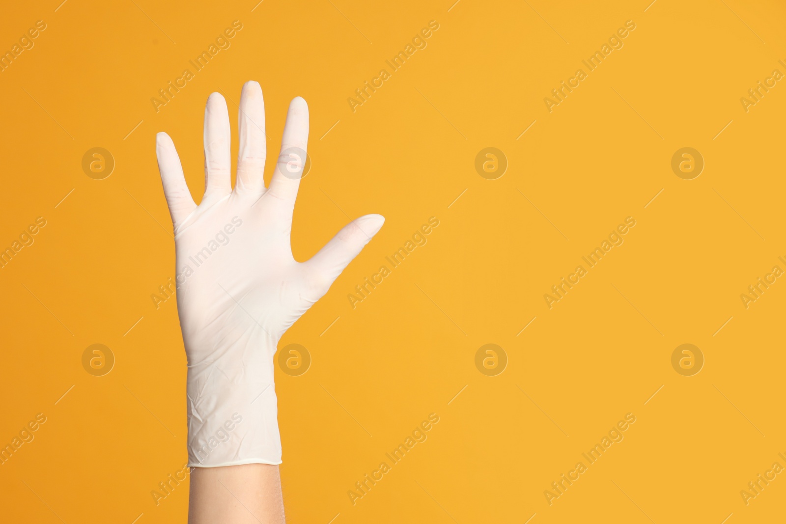 Photo of Doctor wearing medical gloves on yellow background, closeup. Space for text