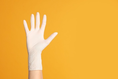 Doctor wearing medical gloves on yellow background, closeup. Space for text