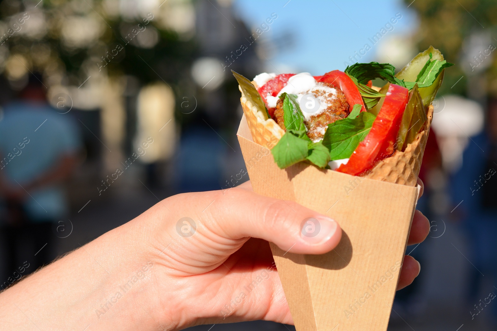 Photo of Woman holding wafer with falafel and vegetables outdoors, closeup. Street food