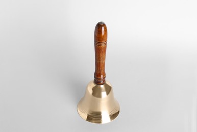 Photo of Golden school bell with wooden handle on grey background