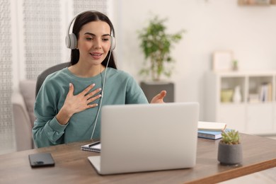 Photo of Young woman in headphones using video chat during webinar at table in room