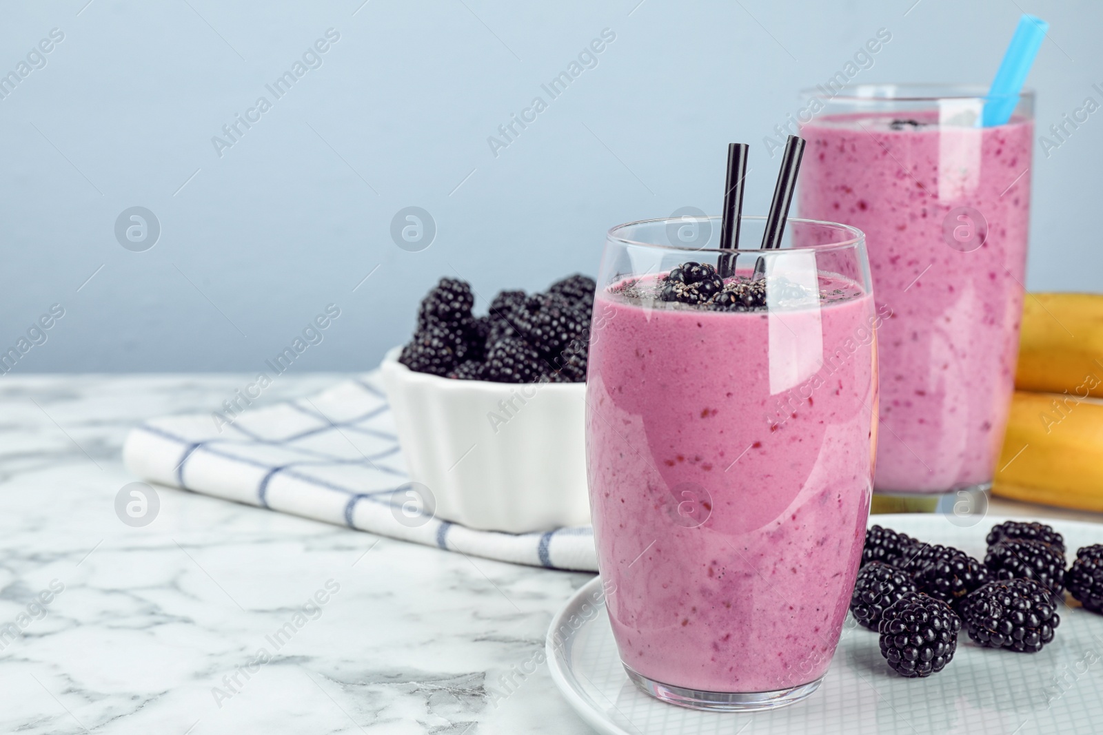 Photo of Delicious blackberry smoothie in glasses on marble table. Space for text