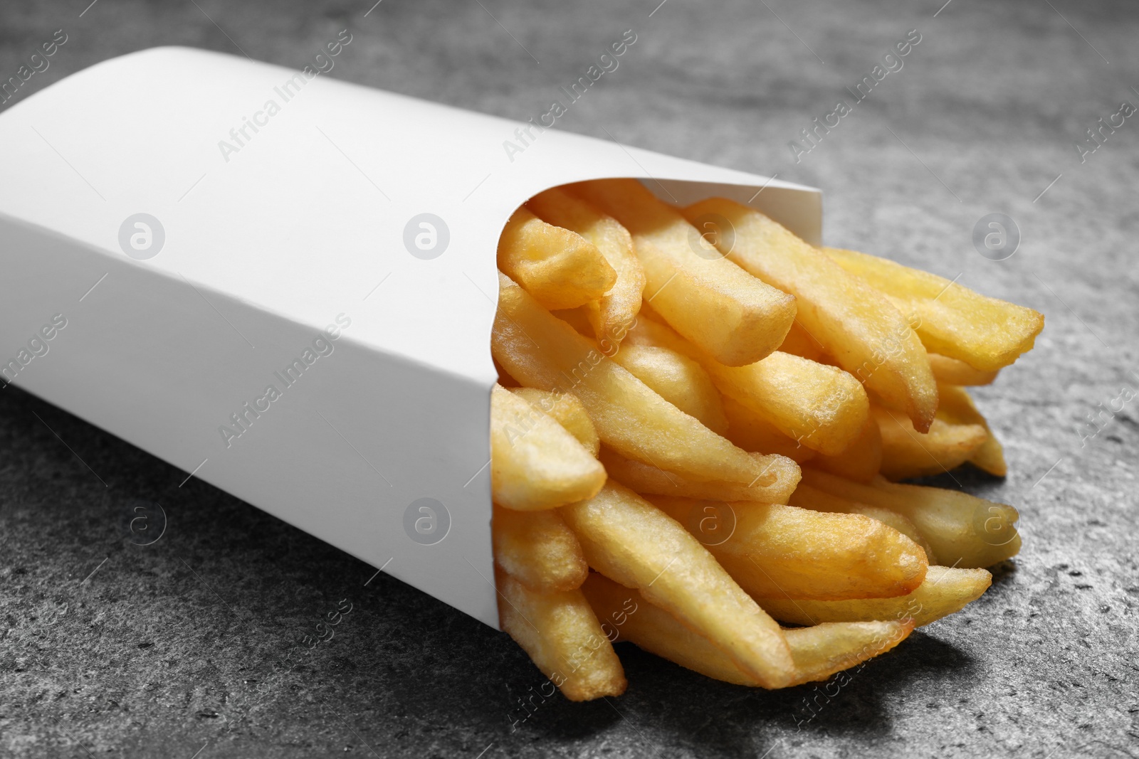 Photo of Delicious french fries in paper box on grey table, closeup