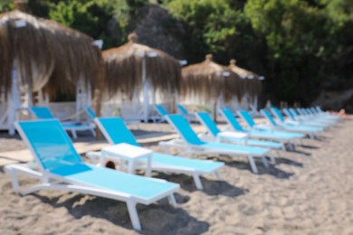 Photo of Blurred view of sandy beach with loungers and huts at resort