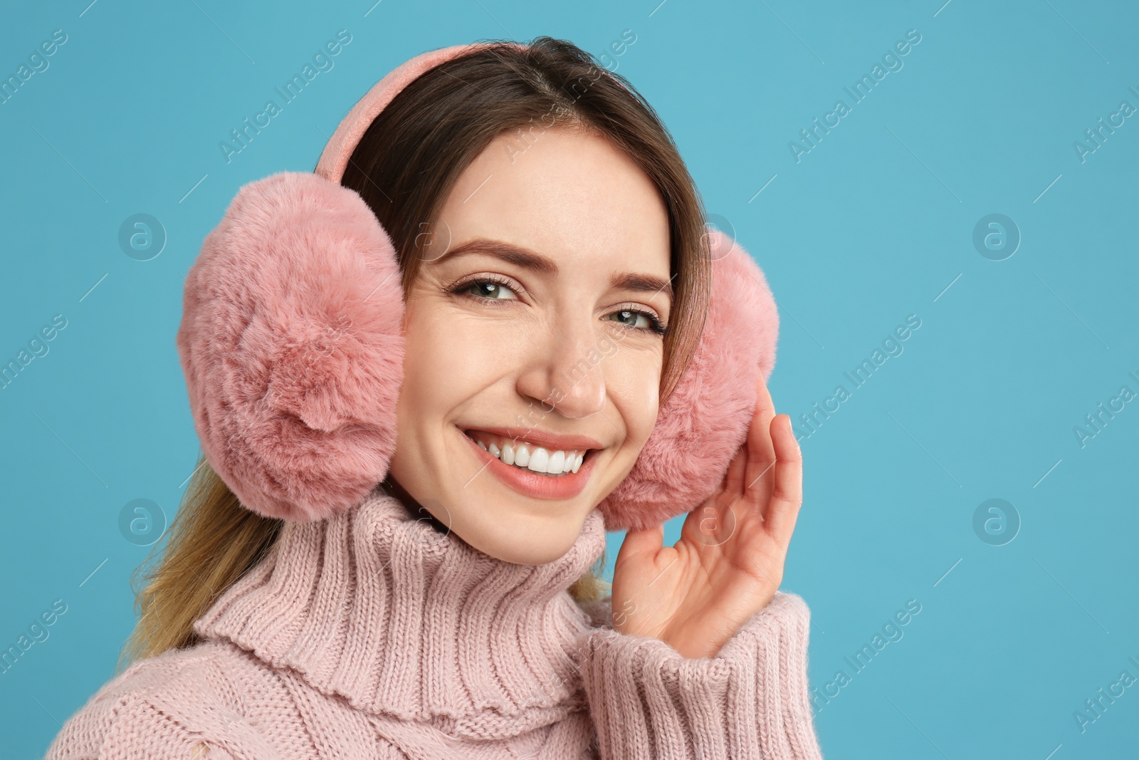 Photo of Happy woman wearing warm earmuffs on light blue background