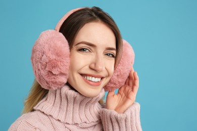 Happy woman wearing warm earmuffs on light blue background