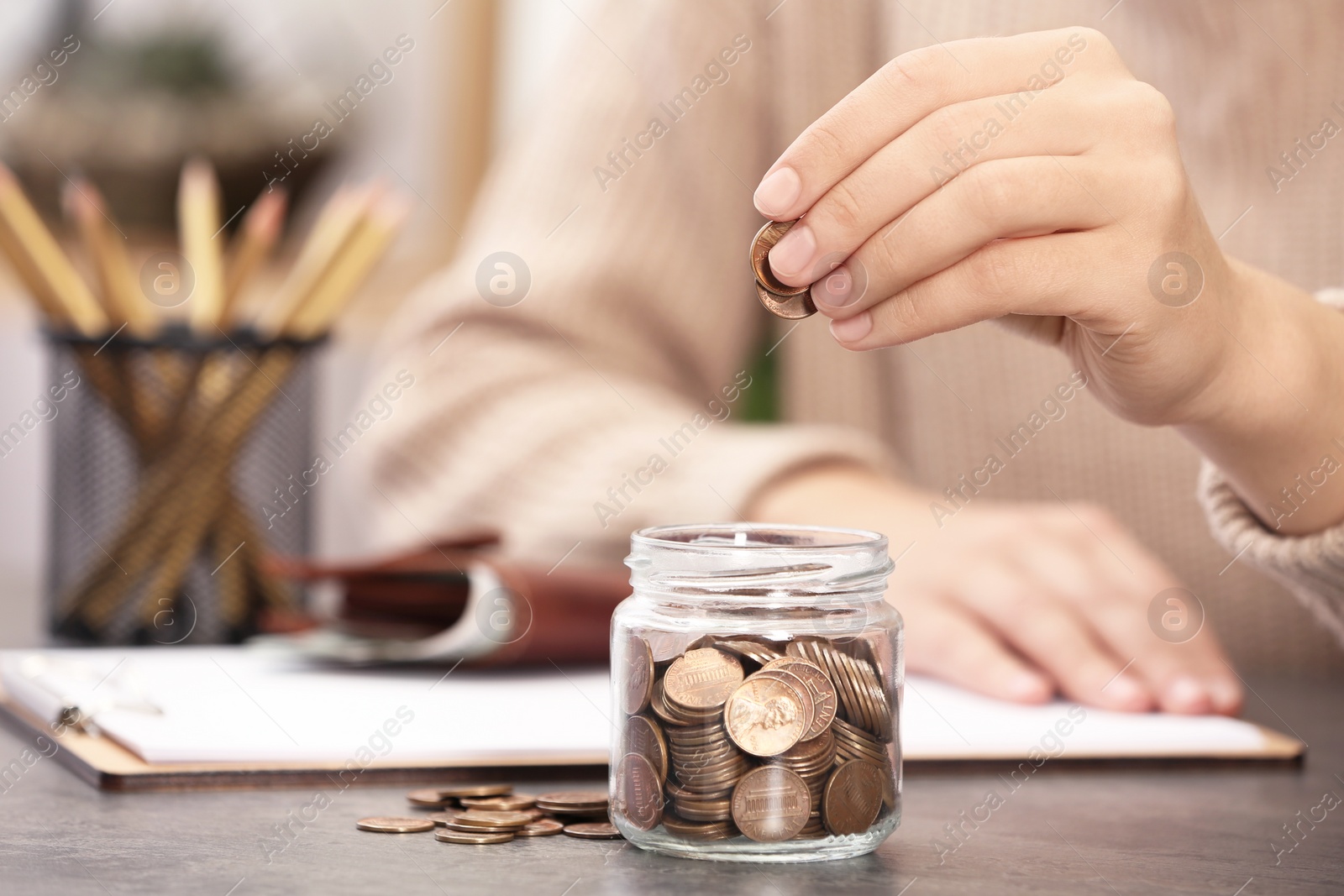 Photo of Woman putting money into glass jar at table, closeup