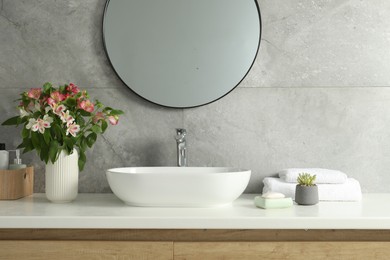 Photo of Vase with beautiful Alstroemeria flowers and toiletries near sink in bathroom