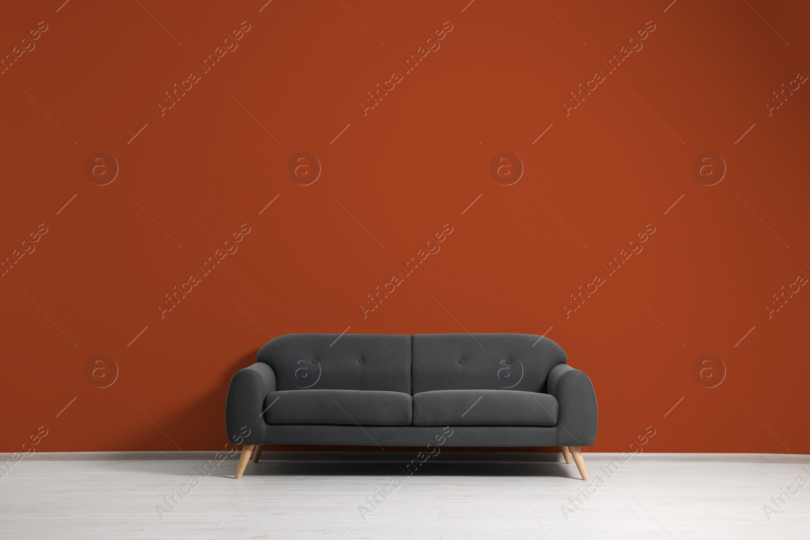 Photo of Stylish grey sofa near dark orange wall indoors. Interior design