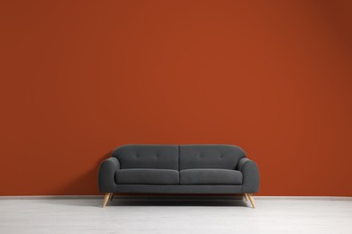 Stylish grey sofa near dark orange wall indoors. Interior design