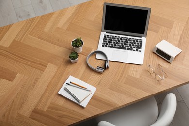 Photo of Wooden table with modern laptop near office chair indoors, above view. Comfortable workplace