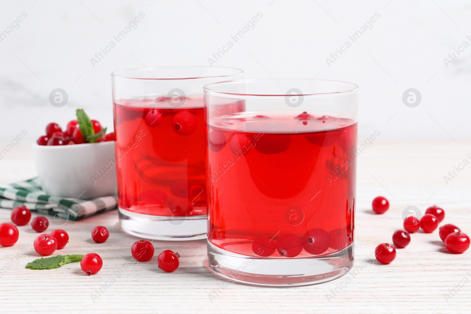 Photo of Tasty cranberry juice in glasses and fresh berries on white wooden table