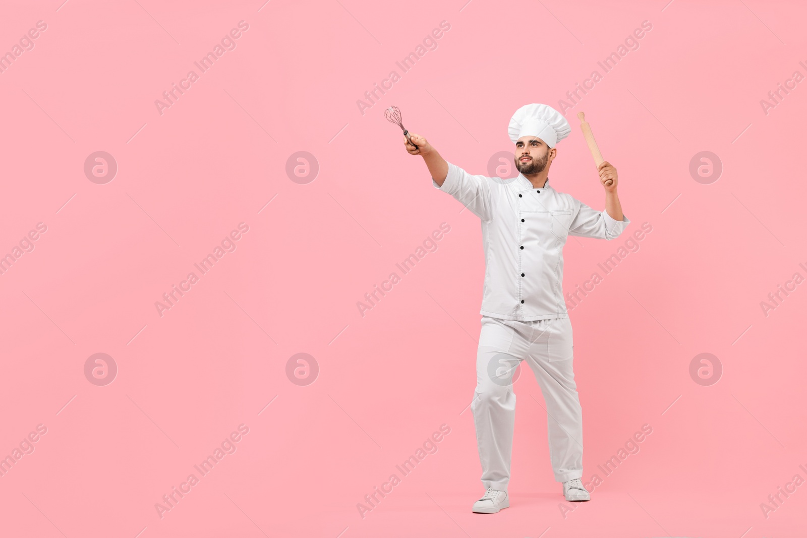 Photo of Professional chef holding kitchen utensils and having fun on pink background. Space for text