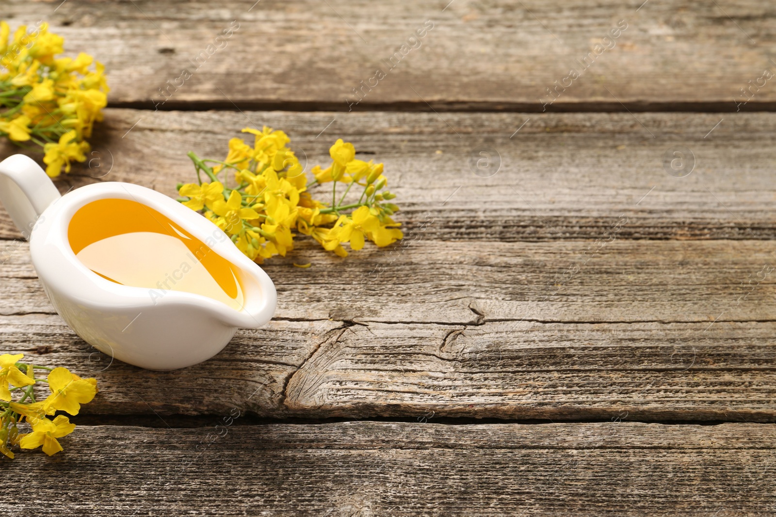 Photo of Rapeseed oil in gravy boat and beautiful yellow flowers on wooden table, space for text