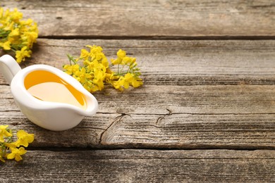Photo of Rapeseed oil in gravy boat and beautiful yellow flowers on wooden table, space for text