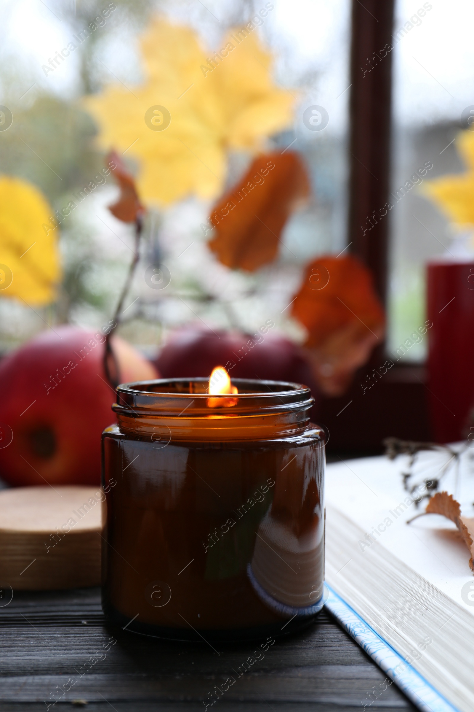 Photo of Beautiful burning candle and book on wooden table. Autumn atmosphere