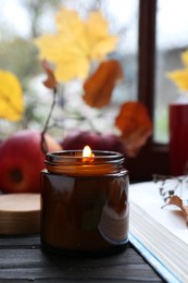 Beautiful burning candle and book on wooden table. Autumn atmosphere