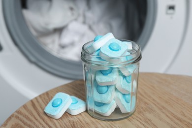 Photo of Jar with water softener tablets on wooden table near washing machine