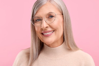 Portrait of beautiful middle aged woman in eyeglasses on pink background