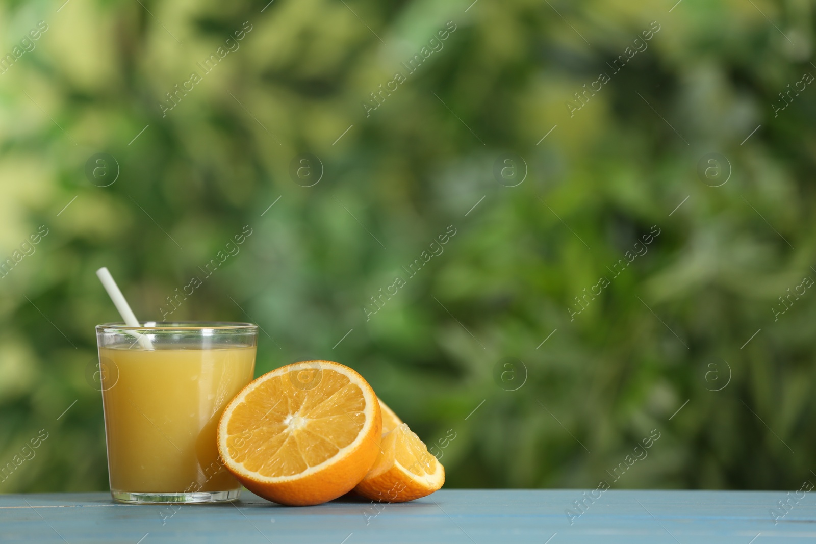 Photo of Delicious orange juice and fresh fruit on light blue wooden table against blurred background. Space for text