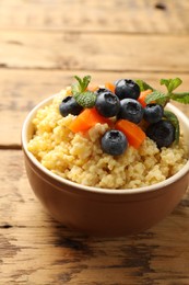 Tasty millet porridge with blueberries, pumpkin and mint in bowl on wooden table