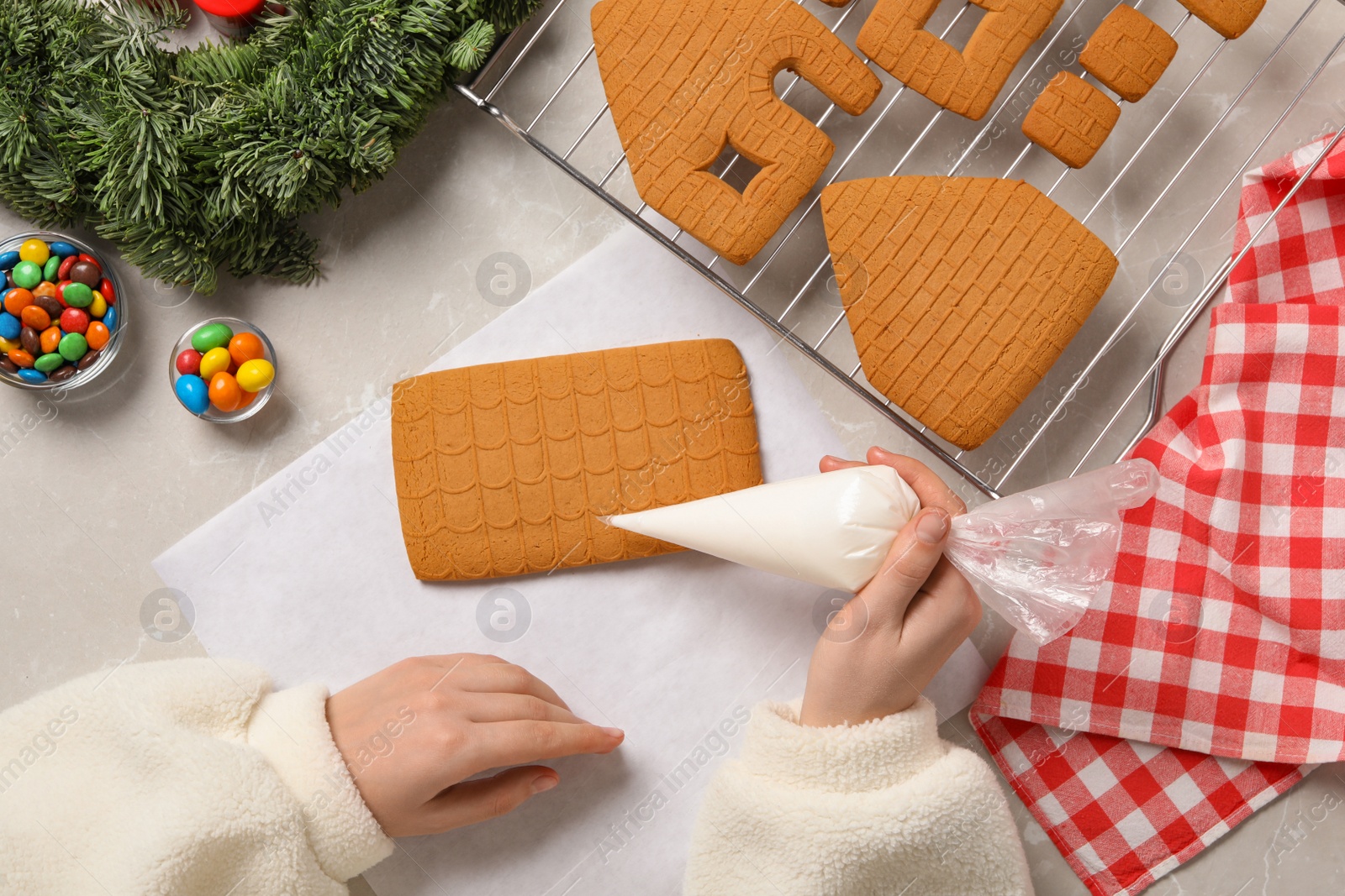 Photo of Woman making gingerbread house at light grey marble table, top view