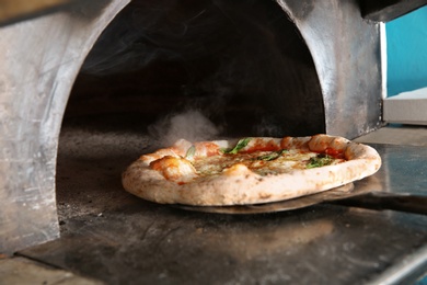 Taking out tasty pizza from oven in restaurant kitchen