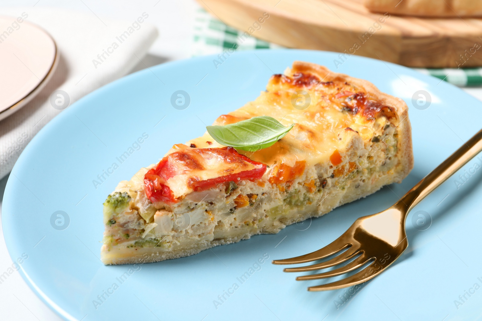 Photo of Piece of tasty quiche with chicken, cheese, basil and vegetables on white table, closeup