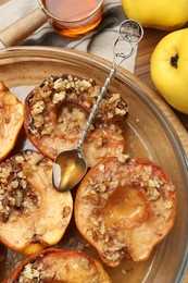Photo of Tasty baked quinces with walnuts and honey in bowl on wooden table, flat lay