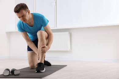 Photo of Man suffering from leg pain on mat indoors. Space for text