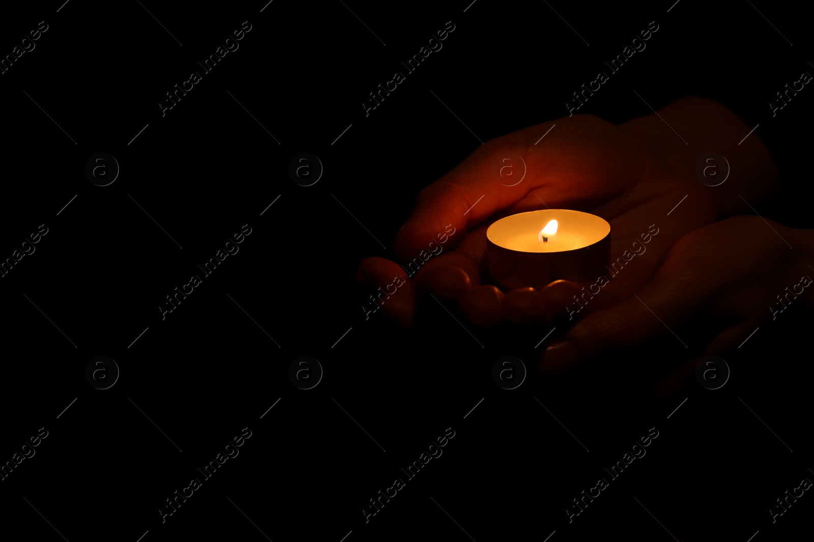 Photo of Woman holding burning candle in hands on black background, closeup. Space for text