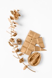 Photo of Shiny golden half of walnut, branch with leaves and chocolate bar on white background, flat lay. Decor elements