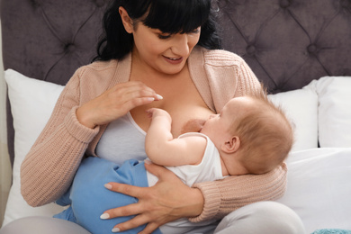 Woman breastfeeding her little baby on bed indoors