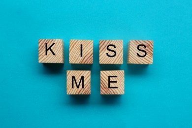 Wooden cubes with phrase Kiss Me on light blue background, flat lay