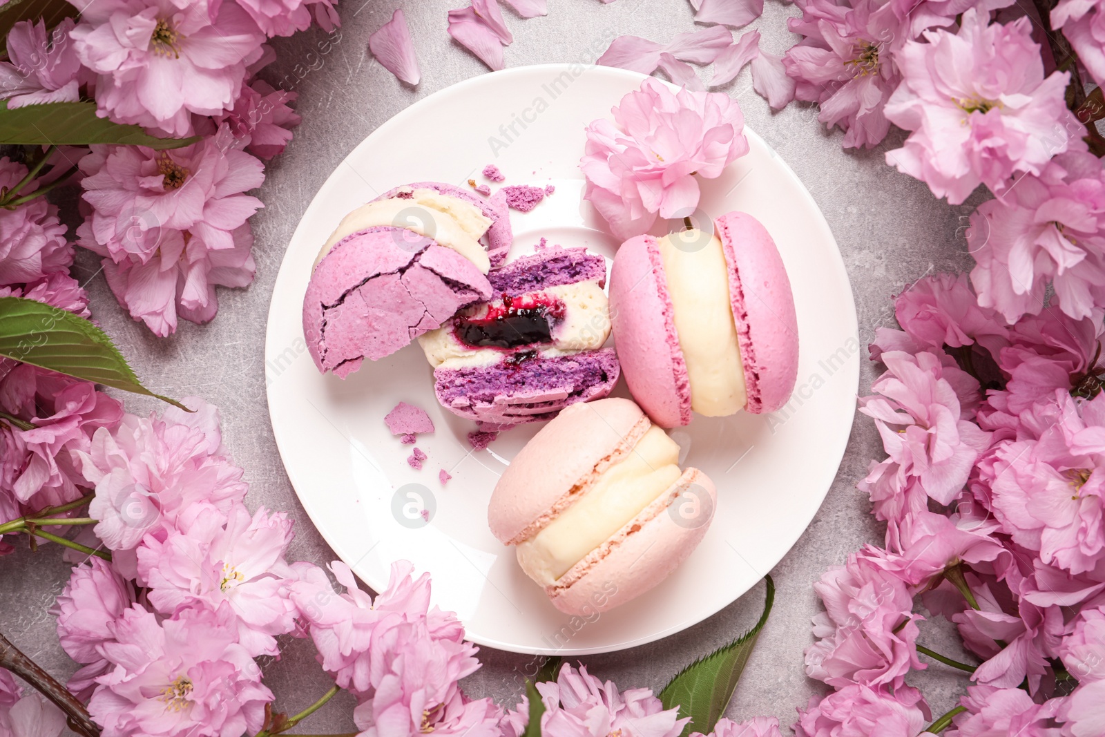 Photo of Delicious colorful macarons and pink flowers on grey table, flat lay