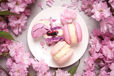 Photo of Delicious colorful macarons and pink flowers on grey table, flat lay