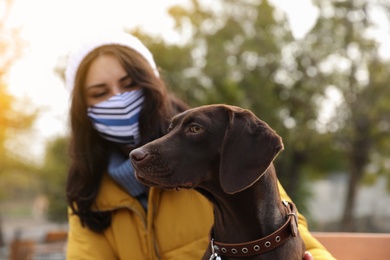 Photo of Woman in protective mask with German Shorthaired Pointer outdoors. Walking dog during COVID-19 pandemic