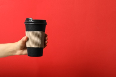 Photo of Woman holding takeaway paper coffee cup with cardboard sleeve on red background, closeup. Space for text
