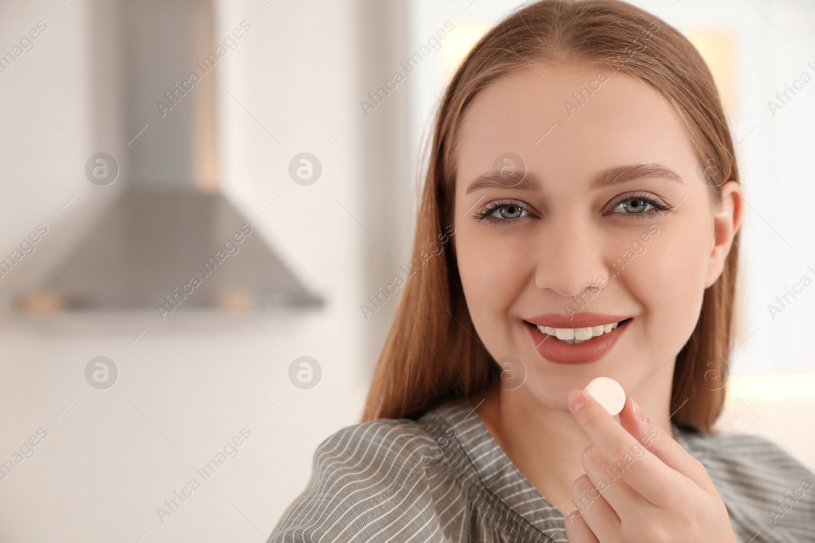 Photo of Young woman with vitamin pill on blurred background. Space for text