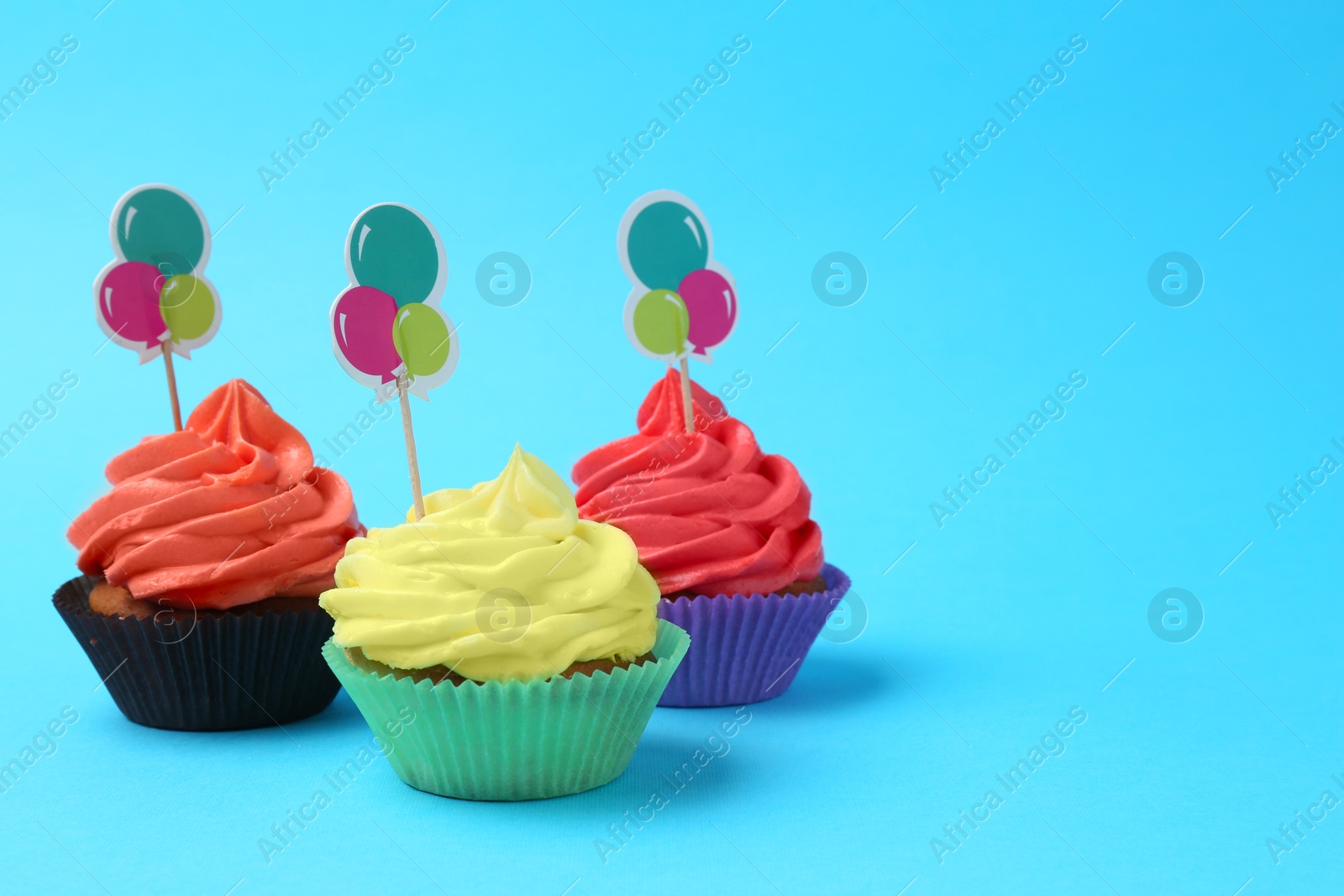 Photo of Delicious cupcakes with bright cream and toppers on light blue background. Space for text