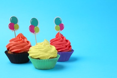 Photo of Delicious cupcakes with bright cream and toppers on light blue background. Space for text