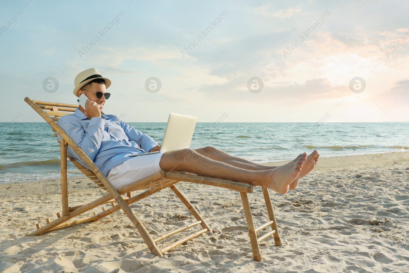 Photo of Happy man with laptop talking by mobile phone on beach. Business trip