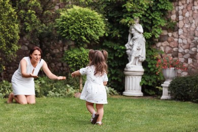 Photo of Cute baby girl making first steps on green grass in park. Mother and her little daughter spending time together