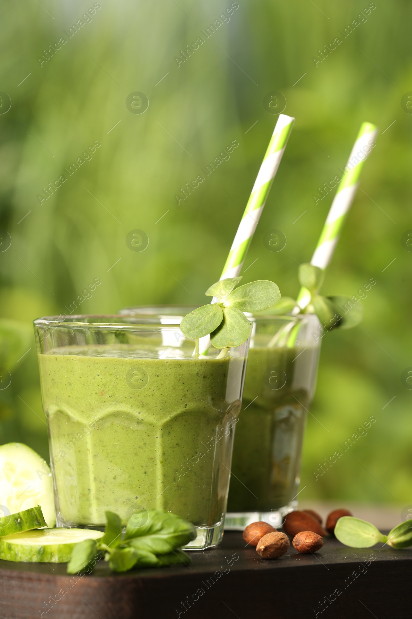 Photo of Glasses of fresh green smoothie and ingredients on wooden table outdoors