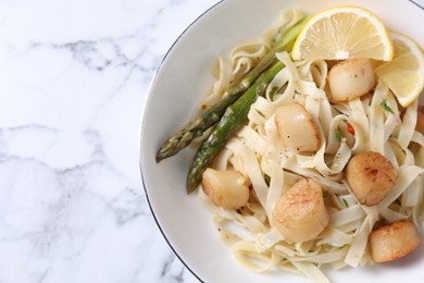 Photo of Delicious scallop pasta with asparagus and lemon on white marble table, top view. Space for text