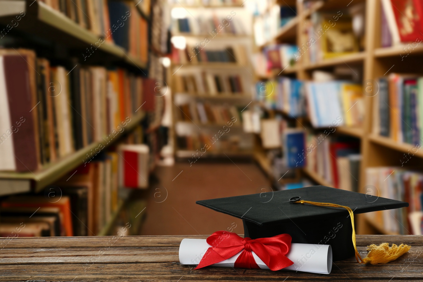 Image of Graduation hat and diploma on wooden table in library, space for text