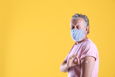 Photo of Cheerful senior man showing arm with bandage after vaccination on yellow background. Space for text