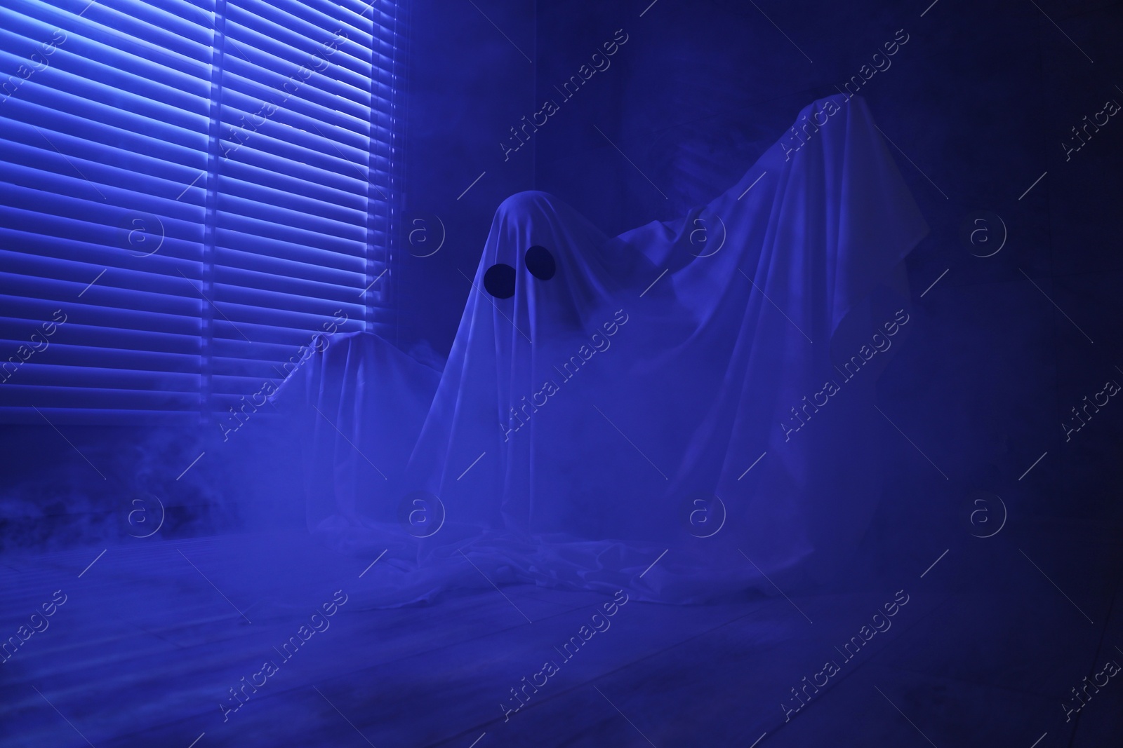 Photo of Creepy ghost. Woman covered with sheet near window in blue light