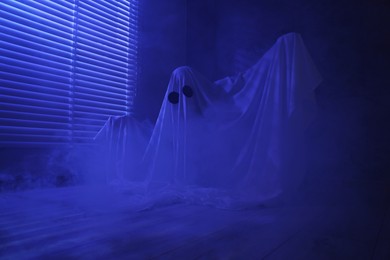 Creepy ghost. Woman covered with sheet near window in blue light